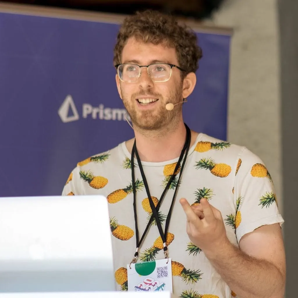 Me smiling and speaking at a conference podium, wearing a pineapples-on-white t-shirt, gesturing with one hand